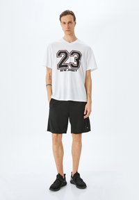 Valkoinen lyhythihainen T-paita, jossa on mustalla painettuna "23" ja "NEW JERSEY". Yhdistetty mustiin urheilushortsieihin ja mustiin lenkkareihin.