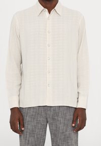 Light beige long-sleeve shirt with thin vertical stripes in blue and gray, featuring a button-down front and classic collar.
