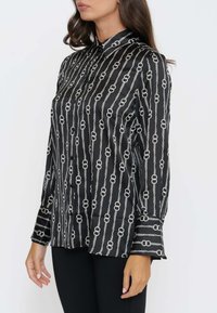 Camicia nera in satin a maniche lunghe con motivo a catena in argento. Presenta un colletto e polsini abbottonati, una texture liscia e una vestibilità dritta.