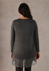 Maglia a maniche lunghe con scollatura rotonda, in tessuto grigio scuro e orlo trasparente. Texture morbida, con una vestibilità leggermente rilassata.