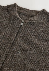 Braun gerippter Strickpullover mit hohem Kragen und silbernem Reißverschlussdetail auf der Vorderseite. Die Textur wirkt weich und gewebt.