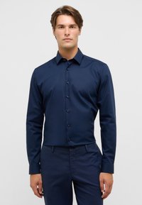 Marineblauwe blouse met knopen, gemaakt van soepele stof, met een klassieke kraag en verborgen knopen, gedragen met bijpassende marineblauwe broek.