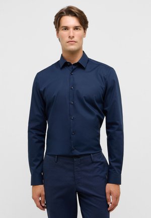 Hemd in Marineblau mit Knöpfen aus glattem Stoff, klassischem Kragen und verdeckten Knöpfen, getragen mit passenden Marineblauen Hosen.