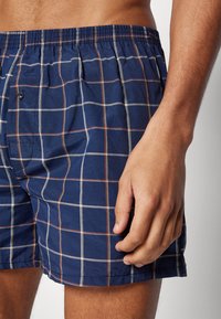 Marineblaue karierte Shorts aus leichtem Material mit elastischem Bund und Knopfdetail, die ein Karomuster in kontrastierenden Farben aufweisen.