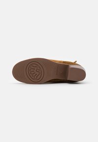 Zapato de ante marrón con suela plana que presenta una suela de goma con diseño y un leve tacón. El diseño incluye una punta redondeada y acentos mínimos.