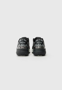 Svart sneakers med en teksturert gummisåle, med et detaljert grått design på baksiden og en logo. Lett konstruksjon og polstret støtte.