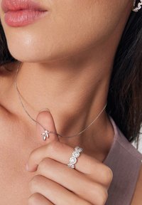 Srebrny naszyjnik z zawieszką w kształcie liścia oraz błyszczącym srebrnym pierścionkiem. Gładkie tekstury i skomplikowane detale są widoczne.