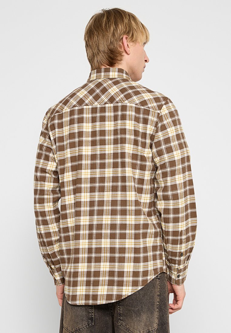 Braun- und gelbkarierte Langarmbluse mit Button-Down-Kragen, einer abgerundeten Säume und kontrastierenden weißen Linien im Muster.