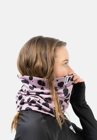 Tour de cou rose à pois noirs, en tissu doux, porté autour du cou. Montre un gros plan du design et de la texture.