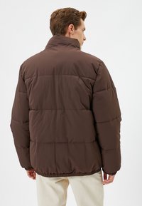 Brun puffy jakke med høj krave, quiltet design og elastiske manchetter. Letvægtsstof, afslappet pasform og en mat overflade.