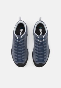 Niebieskie buty wspinaczkowe z teksturowaną tkaniną na cholewce, kontrastującą czarną gumową podeszwą, wyraźnymi sznurowadłami i logo po boku.