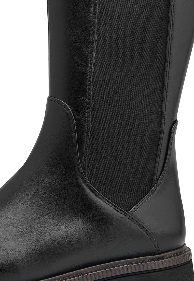 Schwarze Lederstiefelette mit elastischem Seiteneinsatz und braunem genähtem Sohlenrand, die glatte und strukturierte Materialdetails zeigt.
