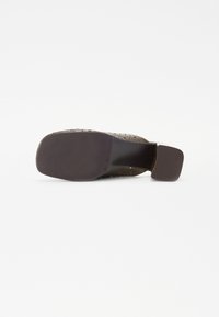 Chaussure perforée marron avec un large talon, surface texturée et semelle lisse. Possède des lignes épurées et un design fonctionnel pour le confort.