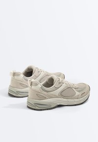 Paire de baskets de sport de couleur beige clair avec des panneaux en maille et en daim, semelles rembourrées et fermetures à lacets, vue de l'arrière en angle latéral.