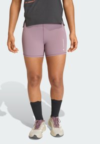 Μωβ αθλητικό σορτς με λεία, ελαστική υφή. Διαθέτει αντανακλαστικές λεπτομέρειες και ραμμένες ραφές. Συνδυάζετ αι με ανοιχτόχρωμα παπούτσια και μαύρες κάλτσες.