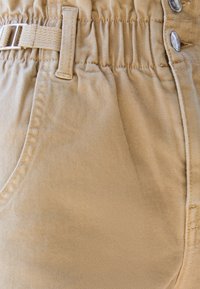Pantalones de algodón beige con cintura elástica, que cuentan con un lazo para cinturón y cierre de botón. Tela texturizada con detalles en los bolsillos delanteros.