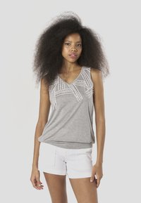 Szürke ujjatlan felső V-nyakkal, fehér geometriai hímzésmintákkal az elején. Fehér rövidnadrággal párosítva, laza megjelenést kölcsönözve.