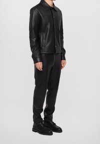 Black leather jacket with a pointed collar, snap buttons, and side pockets, paired with matching black leather pants and boots.