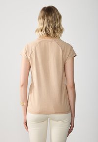 Light beige short-sleeve top with a round neckline and raglan sleeves. Soft fabric with a slightly textured surface. Rear view shown.
