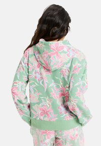Felpa con cappuccio verde chiaro con stampa floreale rosa e bianca. Presenta polsini e orlo a costine, tessuto morbido e una vestibilità rilassata.