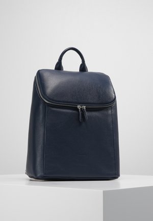 Granatowy plecak skórzany o gładkiej fakturze, prostokątnym kształcie, podwójnych rączkach u góry oraz głównym komorze zapinanej na zamek z frędzlami.