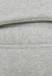 Graues Sweatshirtmaterial mit einer weichen Textur, das sichtbare Nähte und eine glatte, gleichmäßige Oberfläche aufweist. Es sind keine Muster oder Logos vorhanden.