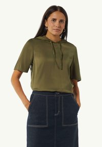 Oliwkowy hoodie z krótkim rękawem i sznurkiem z przodu, sparowany z ciemnoniebieską spódnicą dżinsową z białym przeszyciem i dwoma przednimi kieszeniami.
