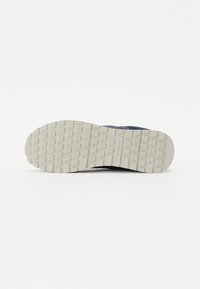 Suola di sneaker con superficie in gomma textured; presenta una suola esterna bianca con una presa a motivo e un componente superiore scuro.