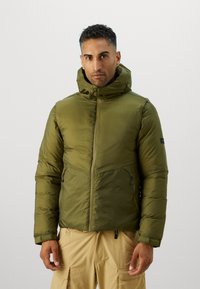 Doudoune vert olive avec un col haut, une fermeture éclair et deux poches avant. Le matériau semble léger et lisse.