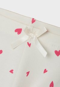 White fabric leggings featuring small pink heart patterns, with a delicate white satin bow at the waist. Soft cotton texture, stretchy design.