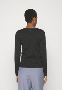 Pull en maille noire avec un motif géométrique, manches longues et ourlet côtelé. Texture lisse et encolure ronde classique.