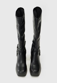 Bottes noires montantes en matériau synthétique lisse, avec une semelle épaisse et des accents de boucle sur les côtés.