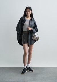 Černá oversized košile, šedý žebrovaný top, šedé kraťasy s kontrastními švy, bílé kotníkové ponožky, černé tenisky, malá kabelka přes rameno.