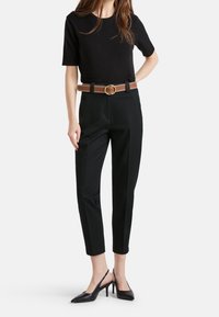 Svart kortärmad topp ihop med avkortade svarta byxor. Brun bälte med cirkulär spänne och kedjedetalj. Svarta slingback-klackar med spetsiga tår.