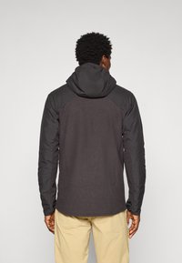 Veste noire avec un dos texturé, des manches lisses et une capuche. Présente des manches raglan et un motif géométrique subtil sur le tissu.
