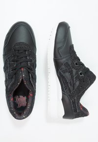 Svarta sneakers med ovandel i läder med en texturerad vävd design, vit gummisula och färgglad innersula med blommönster.