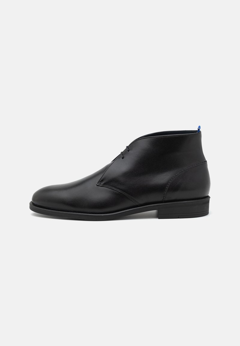 Sorte lær ankle boot med rund tå, minimal søm, og en blå aksent ved hælen. Flat såle for stabilitet. Lett design.