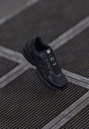 Zwarte sportieve schoen met een bovenwerk van mesh, een textuurdetail, een gevoerde kraag en een rubberen zool. Voorzien van een merklogo aan de zijkant en op de veters.