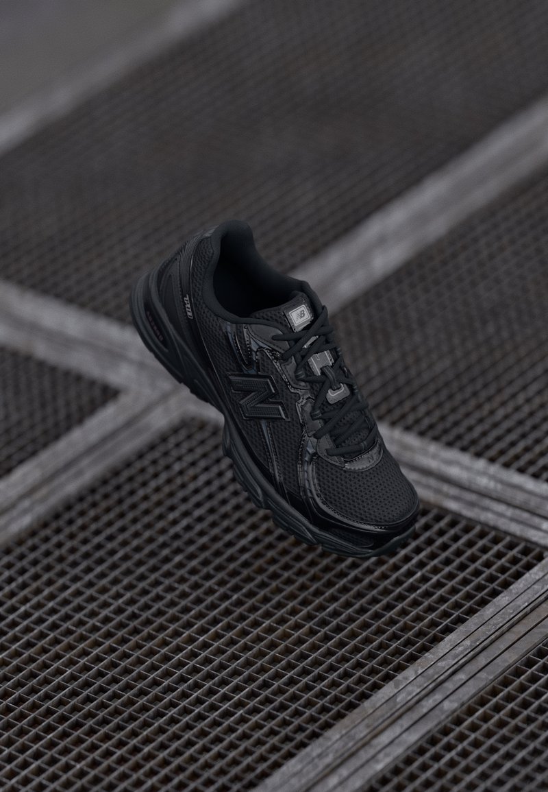 Chaussure de sport noire avec tige en mesh, détails texturés, col rembourré et semelle en caoutchouc. Présente un logo de marque sur le côté et les lacets.