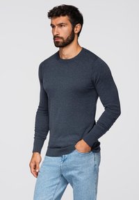 Maglione navy blue a maniche lunghe realizzato in un tessuto texturizzato, con scollatura tonda e polsini e orlo a coste, abbinato a jeans chiari.