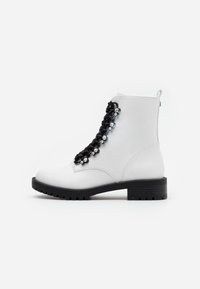 Stivale alla caviglia bianco in pelle con suola spessa nera e lacci neri decorati con piccole borchie a forma di fiore in argento, vista laterale.