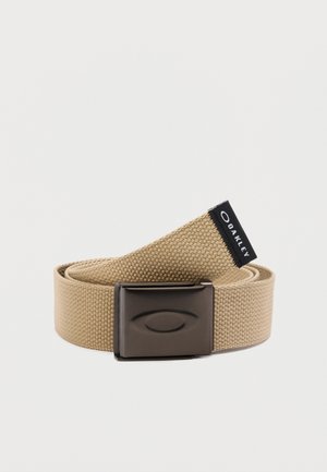 Curea din țesătură bej, cu cataramă din metal închis la culoare, cu un logo oval embosat și o etichetă neagră inscripționată "Oakley".