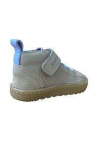 Zapato de ante en color marrón con un tirador y correa de tela azul en el talón. Suela de goma con agarre texturizado. Detalles de costura en la parte superior.