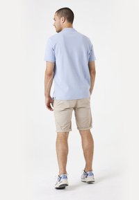 Lichtblauw polo shirt, beige shorts opgerold bij de zoom, sneakers met blauwe accenten. Eenvoudig, casual ontwerp, ontspannen pasvorm.