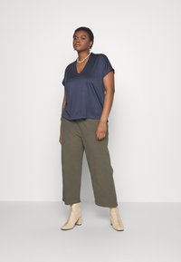Námornícka v-neck tričko s krátkymi rukávmi, v kombinácii s olivovými širokými nohavicami a telovými šnurovacími členkovými čižmami, zvýraznené perlovým náhrdelníkom.