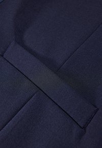 Marineblauem Stoff mit glatter Textur, der über ein rechteckiges Klappendetail verfügt. Das Design enthält dezente Nähte und einen sauberen Abschluss.