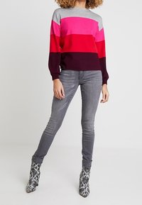 Suéter a rayas colorido en rosa, rojo y gris, combinado con jeans ajustados grises y botas de tobillo con estampado de serpiente. Tejido suave, ajuste relajado.