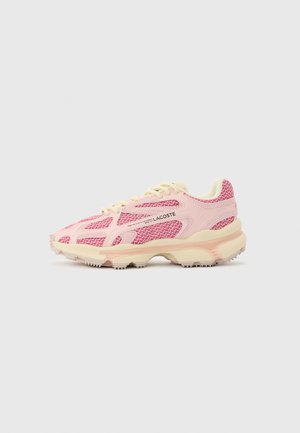 Różowo-beżowy sneaker Lacoste z teksturowaną tkaniną, wiązany na sznurówki, z gumową podeszwą, pokazany z profilu na jednolitym tle.