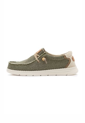Zapato casual de color verde oliva tejido, sin cordones, con detalles beige, cordones elásticos y suela acolchada blanca, mostrado sobre fondo blanco.