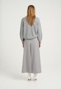 Sivý vlnený sveter s objemnými rukávmi skombinovaný s plisovanou sukňou po zem v sivej farbe. Modelka má na sebe biele lodičky na vysokom podpätku.
